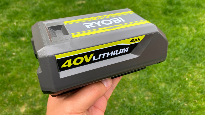 En person holder et lovlig Ryobi-batteri utenfor over en plen.