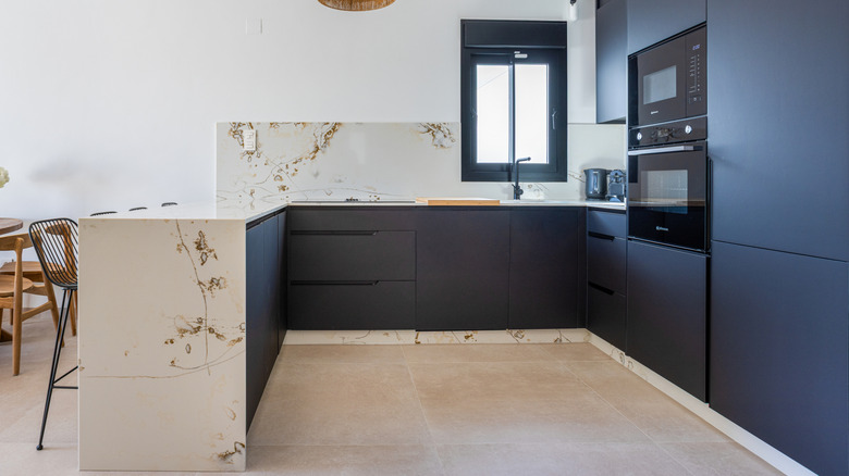 et åpent kjøkken med mørke skap og storformat fliser på gulv