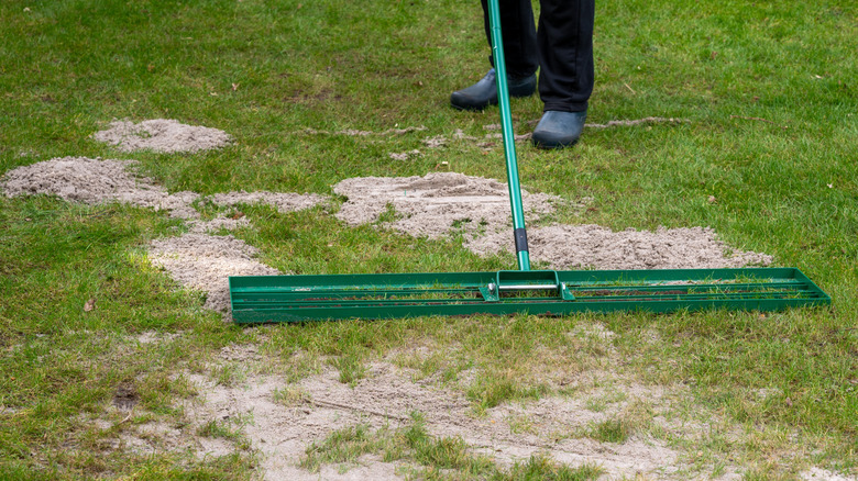 Person som bruker en stor rive for å legge sand på plenen