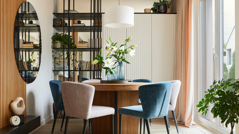 Moderne spisestue med rundt trebord, blå og hvite polstrede stoler og veggspeil.