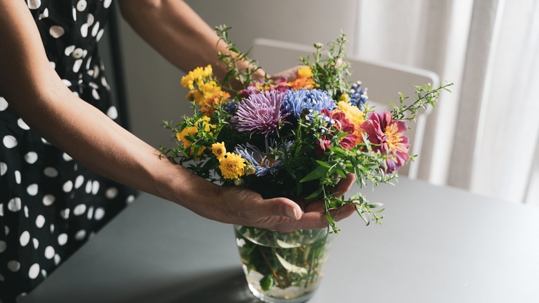 Nærbilde av hender som arrangerer blomster i en glassvase