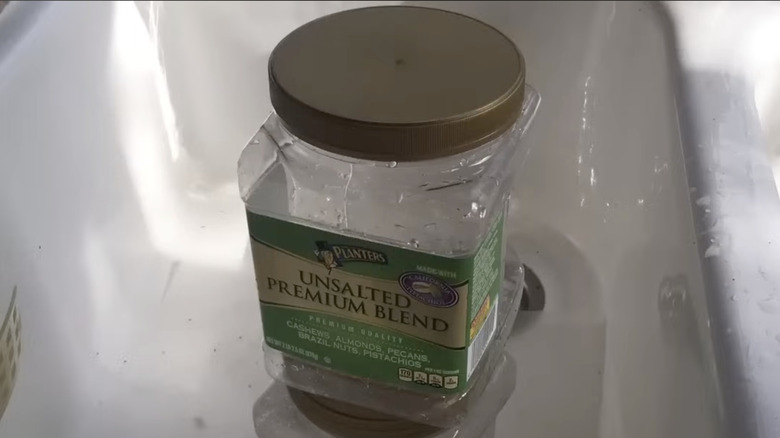 En tom plastbeholder med usaltede nøtter med et stort gulllokk i en kjøkkenvask.