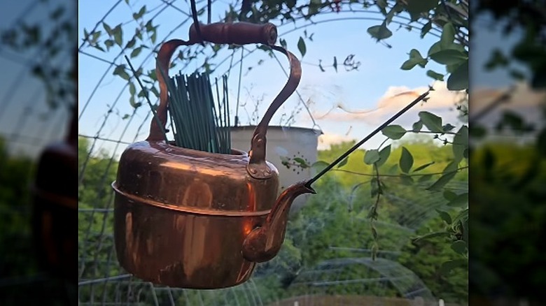 En kobberkjele hengende på en krok som holder citronella-pinner i toppen med en brennende pinne i tuten.