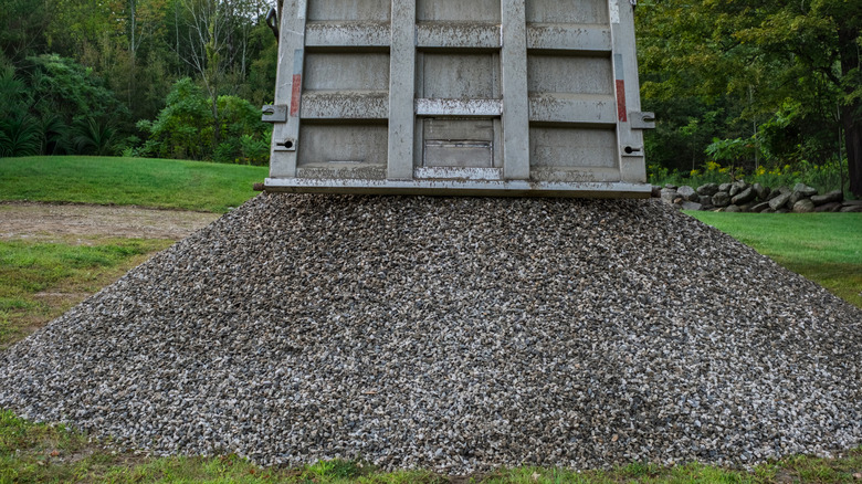 En dumper laster av en steinhaug i en gresskledd hage.