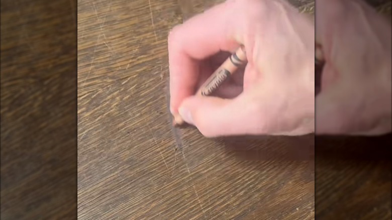 Hånd gnir en brun fargestift på en beis på tregulv