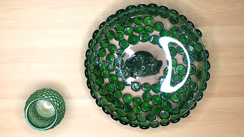 En liten grønn vase ved siden av en bolle dekket av grønne glassperler på undersiden med en froskefigur i midten