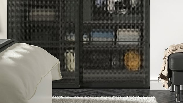 Et soverom med innebygget svart skap med rutete glass LUNDBRÄSMA-paneler som viser gjenstander innvendig.