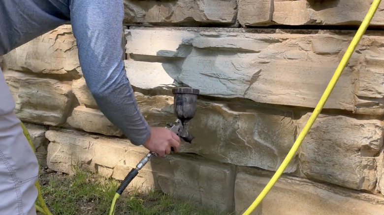 En mann sprayer flekk på støttemur av betongblokk.